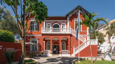 EF Language Abroad students walking and gathering outside a historic red campus building in Málaga, Spain, surrounded by palm trees and outdoor seating areas.