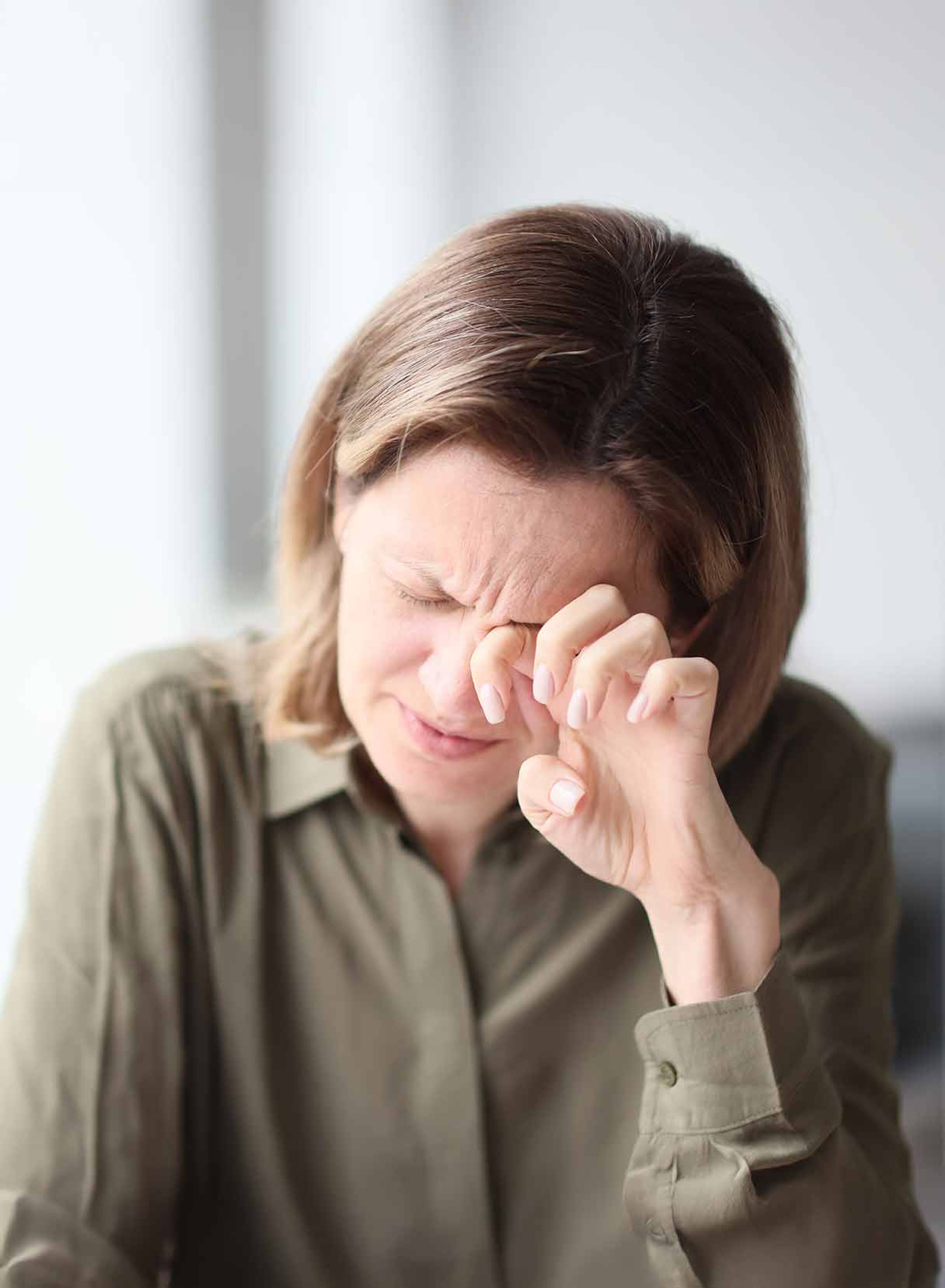 Donna in camicia verde strofina il suo occhio secco.