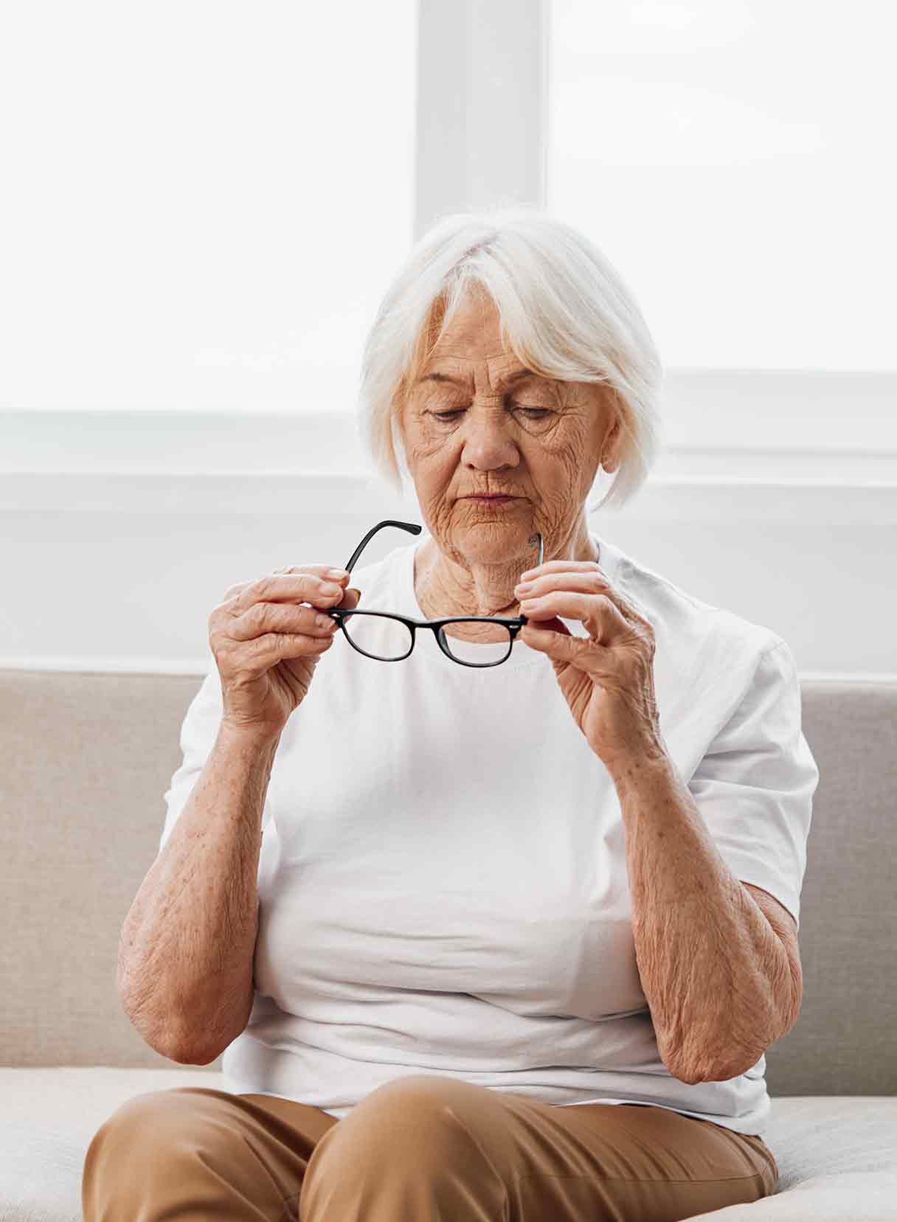 donna anziana con cataratta matura guarda gli occhiali che regge con le mani