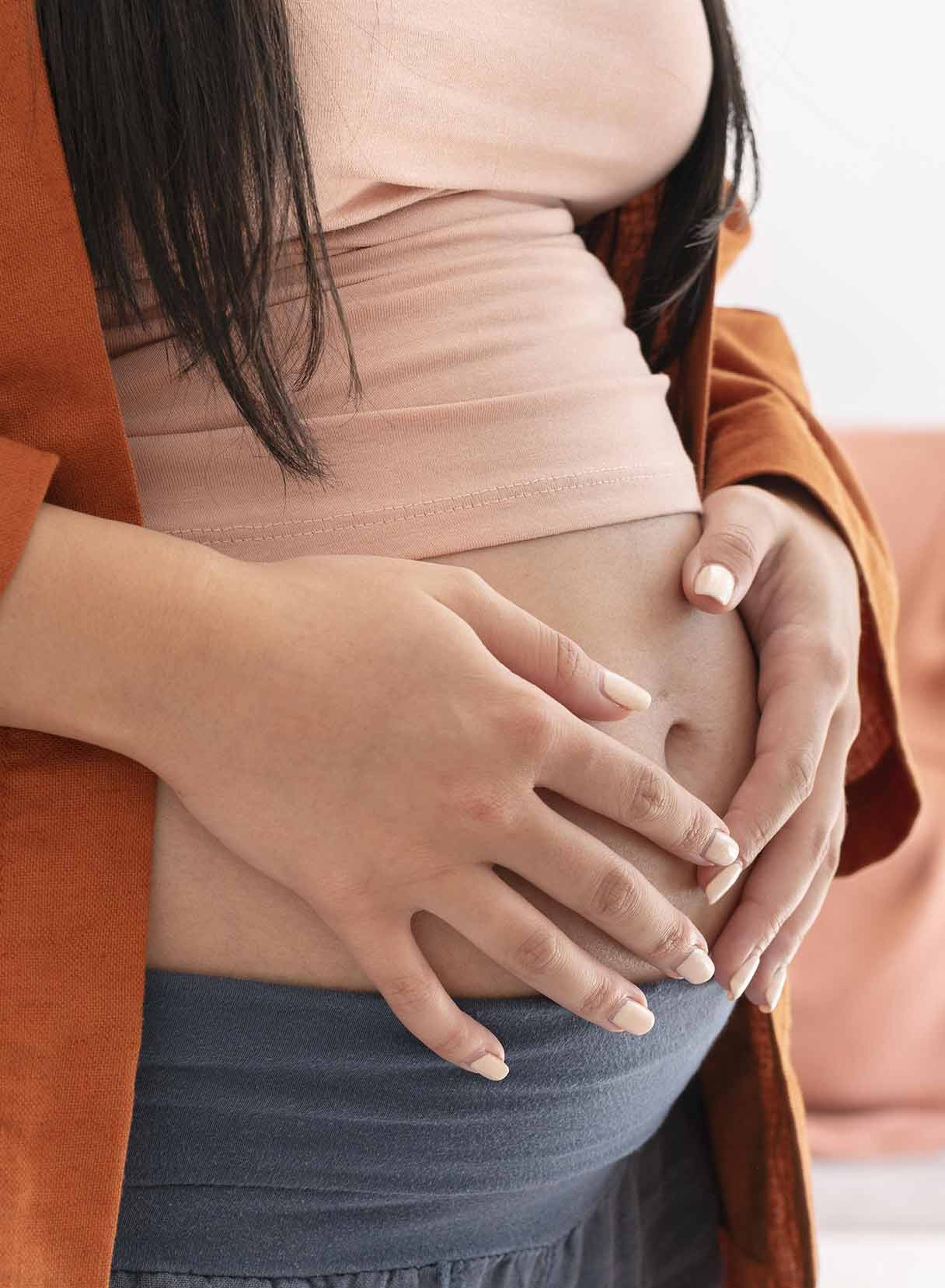 Donna incinta con top rosa e cardigan arancione si culla la pancia con entrambe le mani