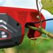 Close-up of a red electric tool trimming a green plant branch outdoors, with a blurred background and visible leaves.