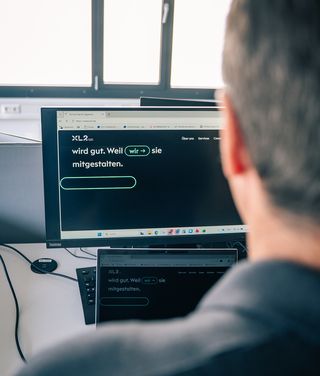 Mann mit Brille arbeitet fokussiert am Laptop in modernem Büro mit Neon-Beleuchtung