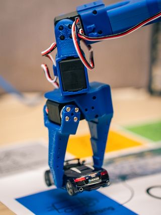 Blauer Roboterarm greift bei einem AI-Robotics-Demonstrator ein Fahrzeugmodell