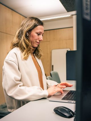 Fachfrau arbeitet konzentriert am Laptop in modernem Büro mit Holzwänden und LED-Beleuchtung