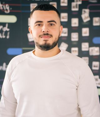 Sinan Celik vor unscharfem Tech-Hintergrund mit Netzwerk-Grafiken