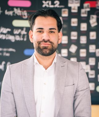 Gabriel Elias im grauen Blazer vor einer digitalen Tafel mit technischen Diagrammen