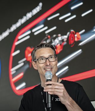 Mann mit Brille präsentiert vor digitalem Display mit Datenvisualisierungen und spricht ins Mikrofon