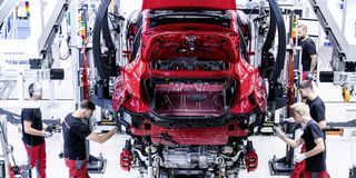 Workers assembling a red car on a modern automotive production line.