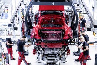 Workers assembling a red car on a modern automotive production line.