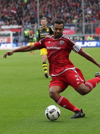 Fußballspieler in Rot dribbelt Ball auf Rasenplatz während Stadionmatch