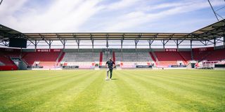 Person steht allein auf Fußballplatz mit modernem Stadion im Hintergrund
