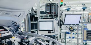 Car assembly line with open-hood vehicle and diagnostic equipment.