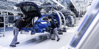 Zwei Arbeiter montieren ein blaues Auto in einer hochmodernen Fabrik mit automatisierten Fertigungsanlagen und Roboterarmen