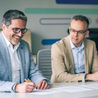Zwei Professionals arbeiten gemeinsam an Projektdokumenten mit digitalen Elementen im Hintergrund