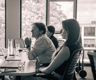Vier Personen bei einer Besprechung mit Laptops in einem hellen Konferenzraum