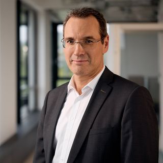 Porträt Bernd Borberg im dunklen Anzug und Brille in modernem Bürogebäude mit Glaswänden