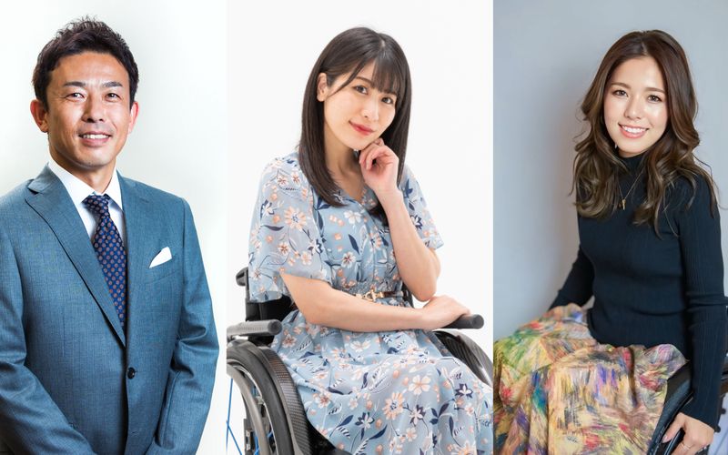 Three people posing against a plain background, including a man in a suit and two women in wheelchairs wearing a floral dress and a black top with a colorful sk