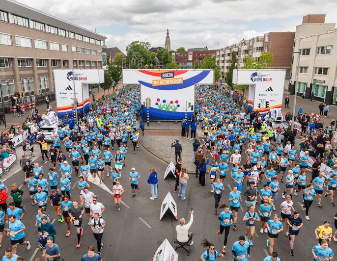 Hundreds of runners in blue shirts start the Wings for Life World Run in Breda under a large event arch surrounded by cheering crowds.
