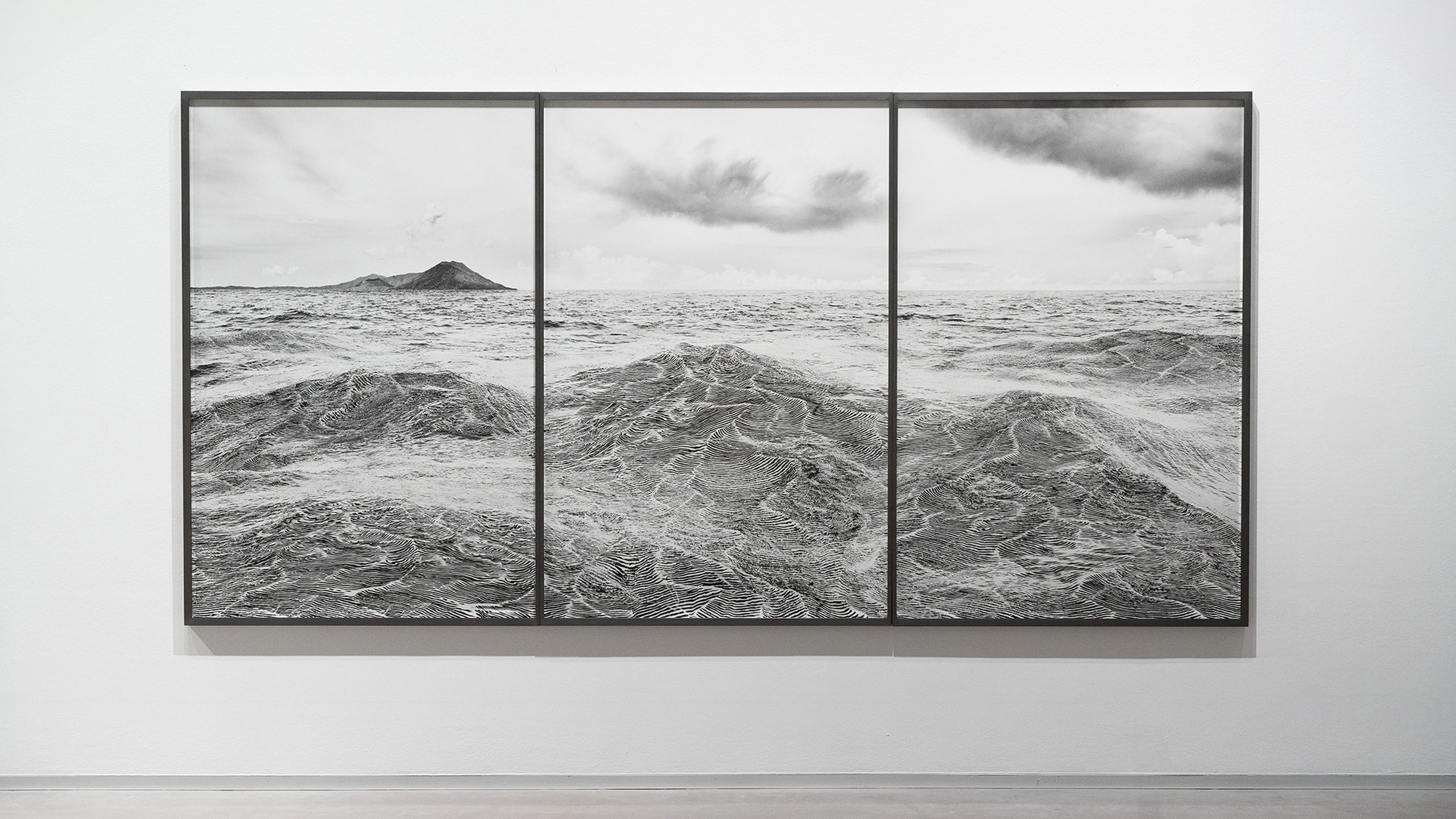 Triptych of black and white ocean photography showing turbulent waves and a distant mountainous island under a cloudy sky.