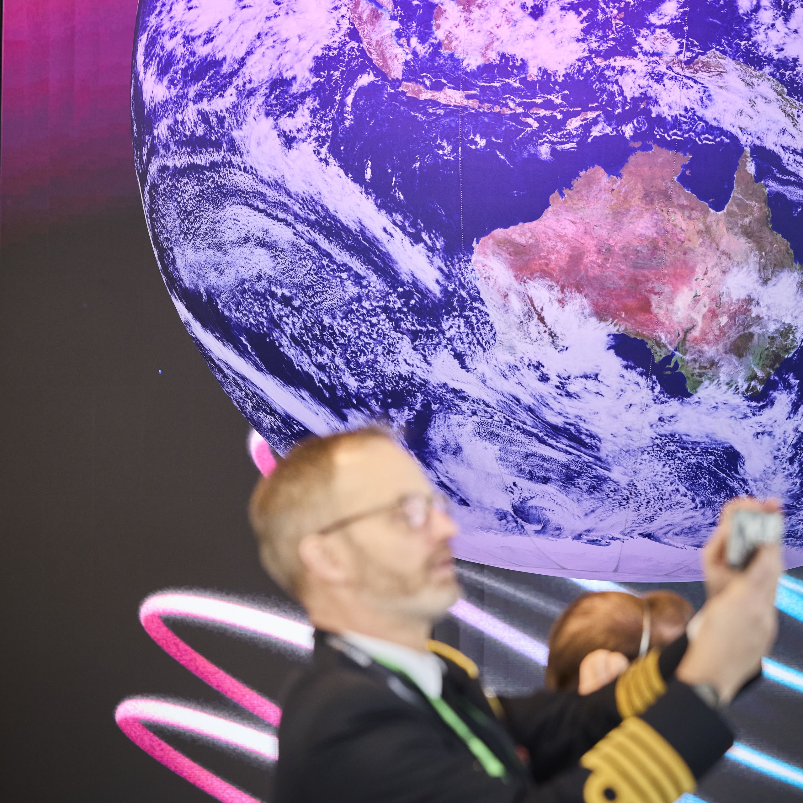 A person takes a photo in front of a large screen displaying Earth from space, with the BMW Foundation logo visible.