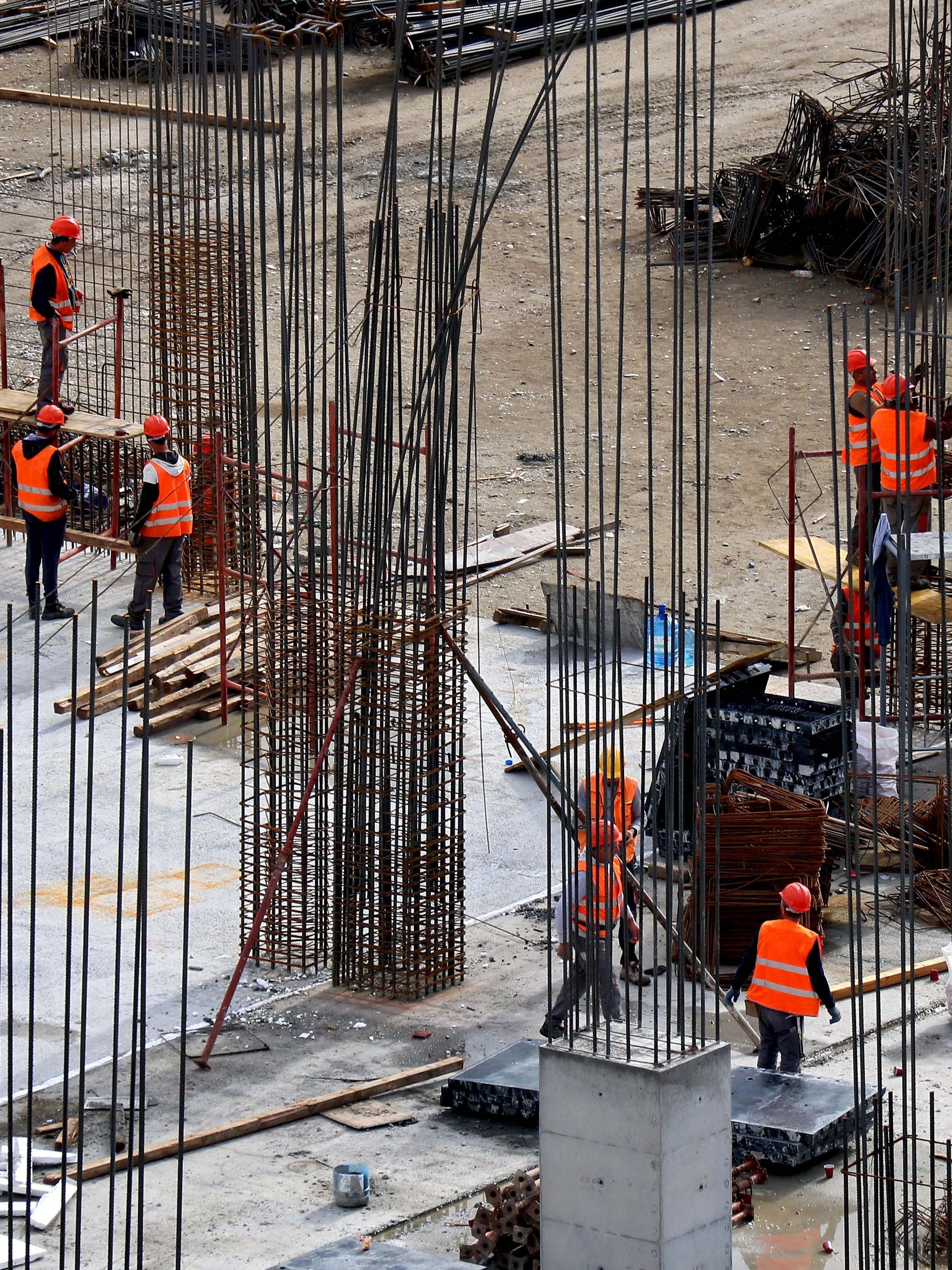 Construction site with workers in orange vests and helmets, surrounded by steel rods and concrete pillars, on a partially completed building. Construction site with workers in orange vests and helmets, surrounded by steel rods and concrete pillars, on a partially completed building.