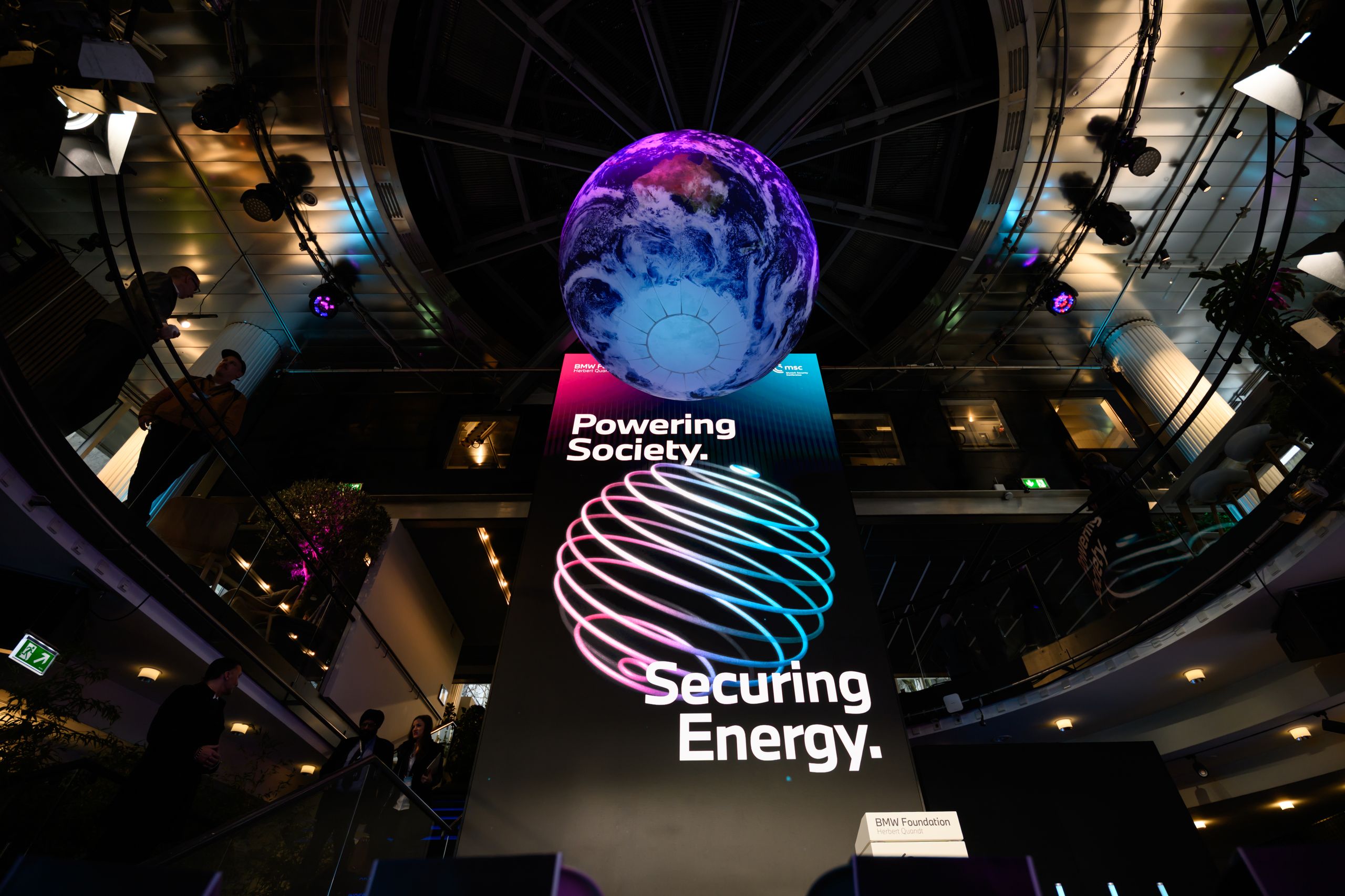 A large digital display with text "Powering Society. Securing Energy." beneath a glowing globe, set in a modern interior with ambient lighting.