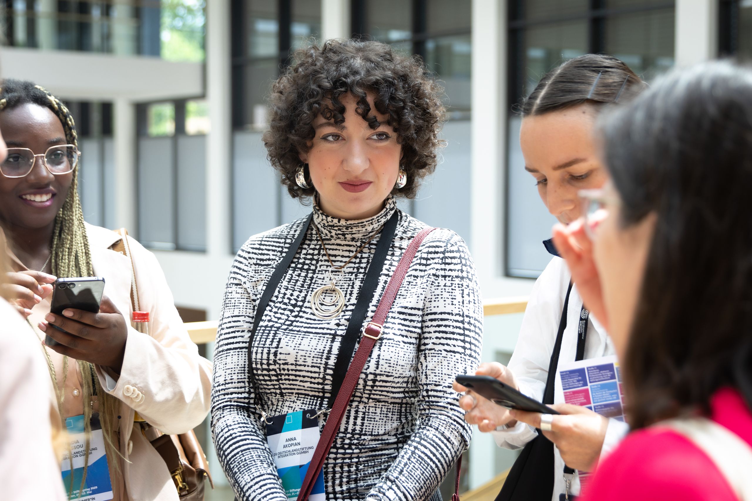 A group of four people engaged in conversation, holding smartphones and name tags, in a bright indoor setting.
