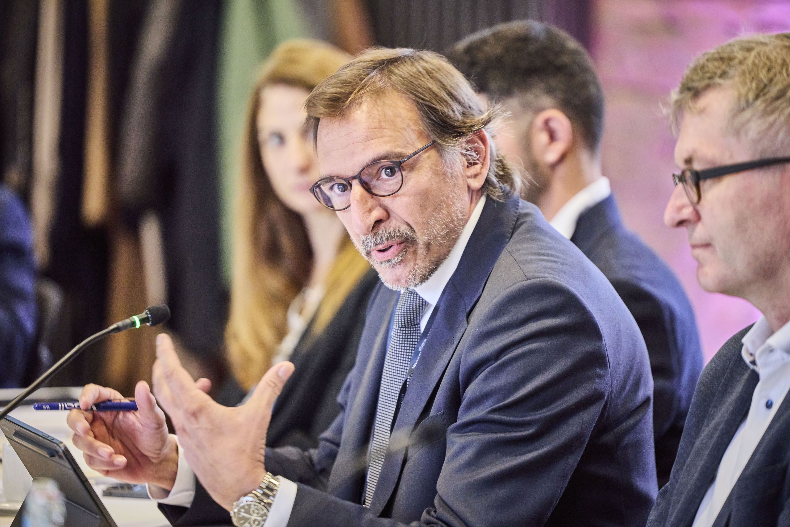 Ignasi López Verdeguer, Director of Science engagement and Strategy at Fundación ”la Caixa”. Man in a suit speaking passionately at a conference table, surrounded by other people listening.