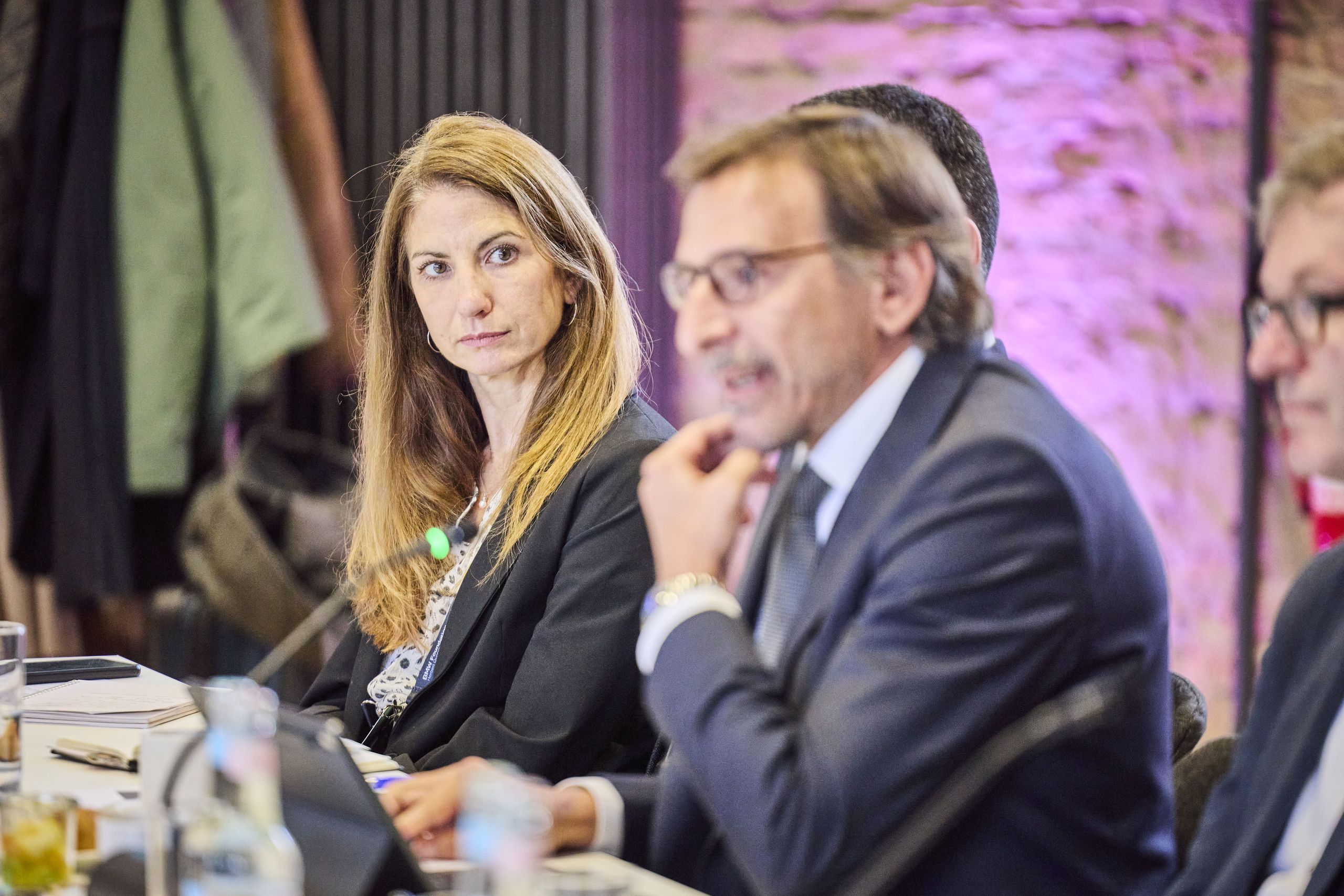 Kathy Nothstine, Director Future Cities at Nesta. A woman listens attentively while a man speaks at a conference table with documents and glasses of water.