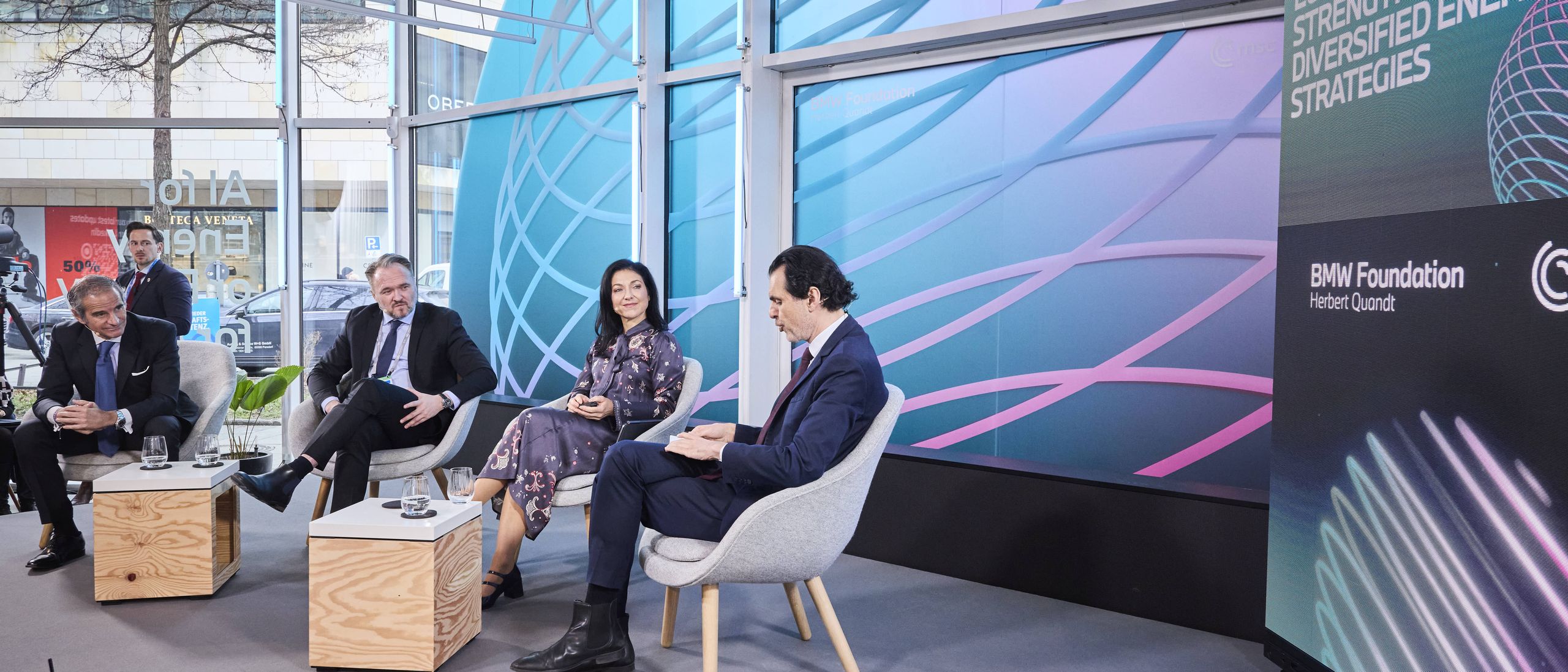 Four people engaged in a panel discussion on energy matters, seated on a stage with a large screen displaying the event theme in the background.