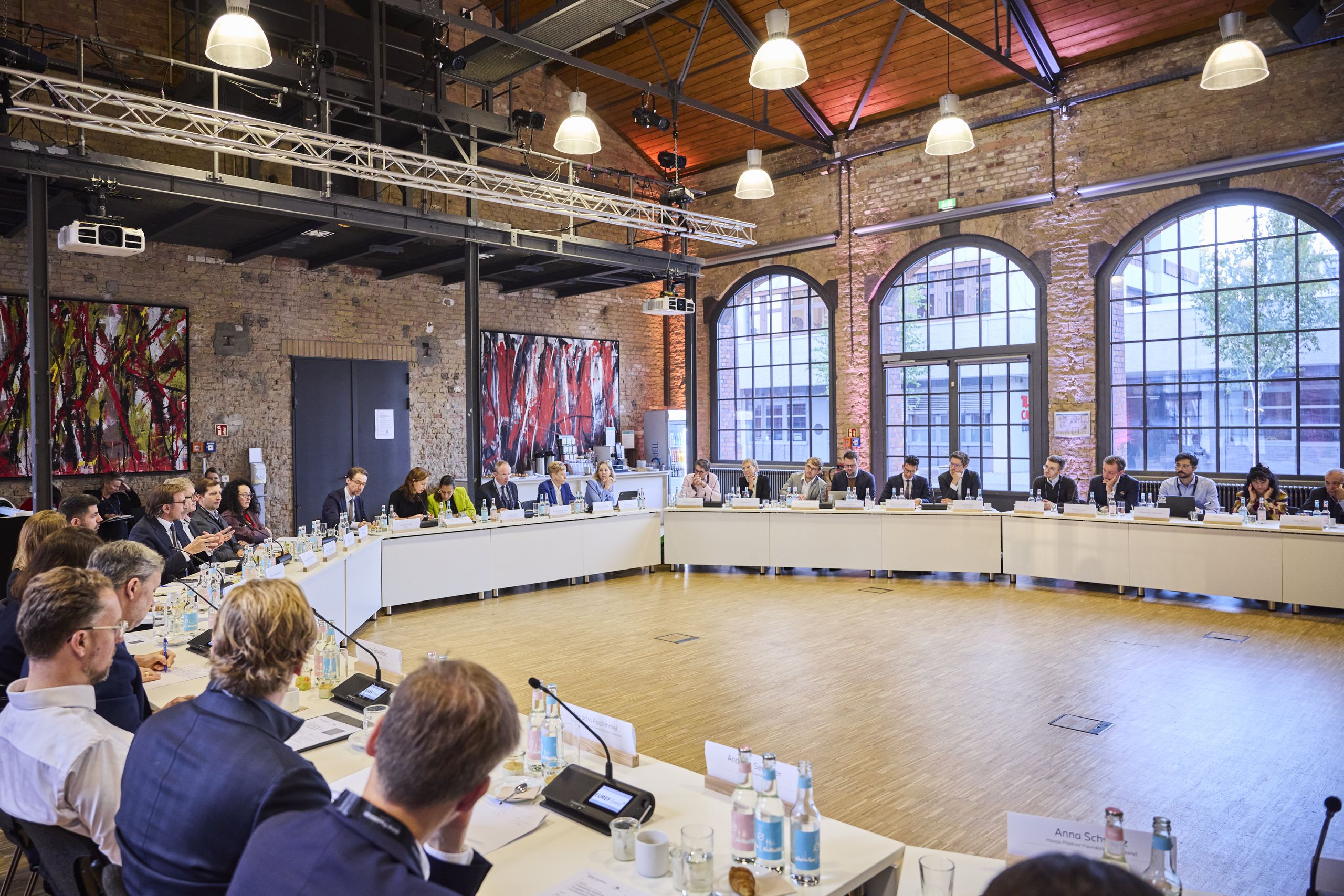 The session was part of the BMW Foundation's Leaders Collaboration Forum 2026 in Berlin. A large group of people are seated around a circular conference table in a spacious room with brick walls and large arched windows.