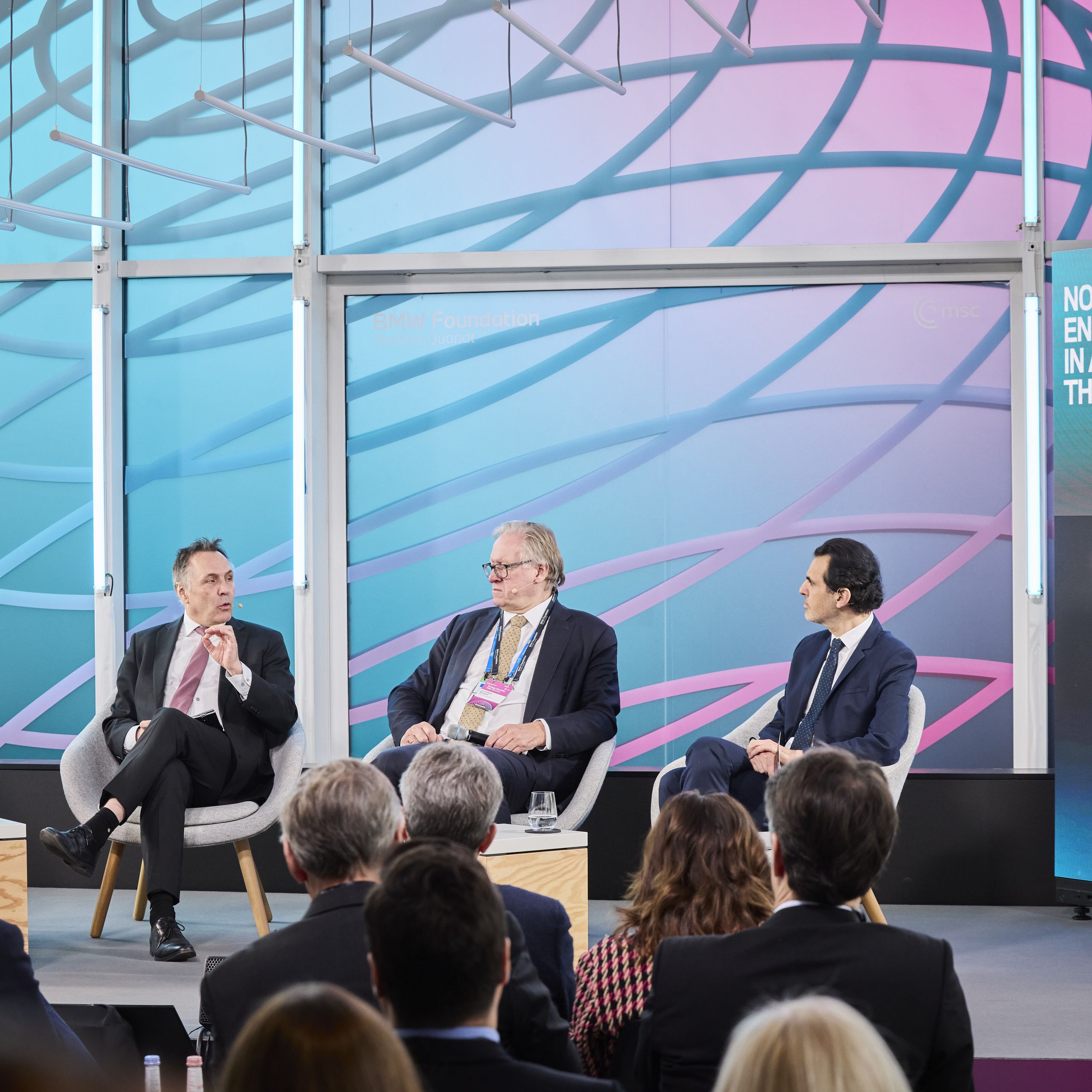 Four men in suits seated on stage discussing energy security in the Arctic, with a colorful abstract backdrop and audience in front.