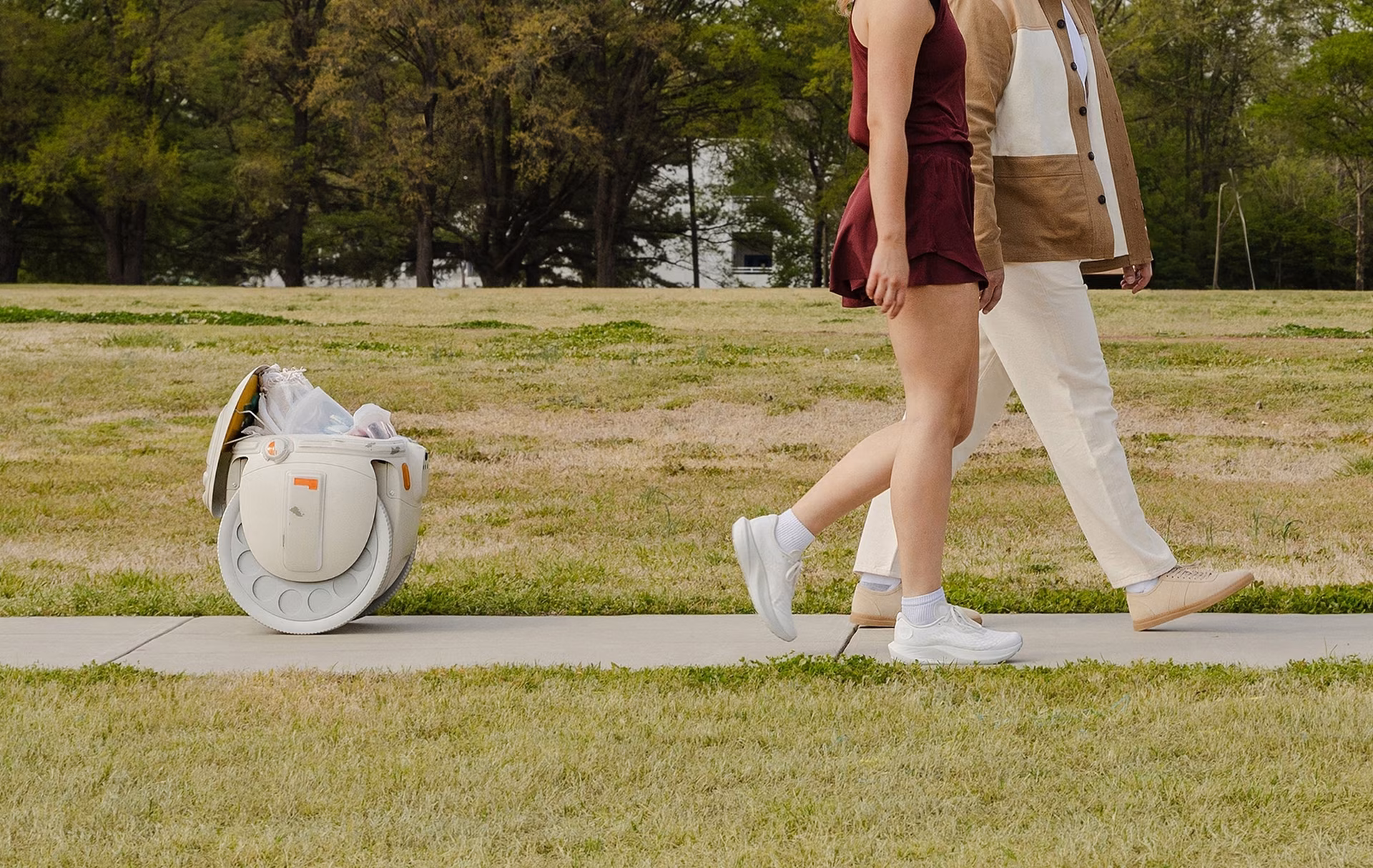 Wide shot side view image of the Grogu™ gitamini robot following behind a father and daughter as they're walking outdoors