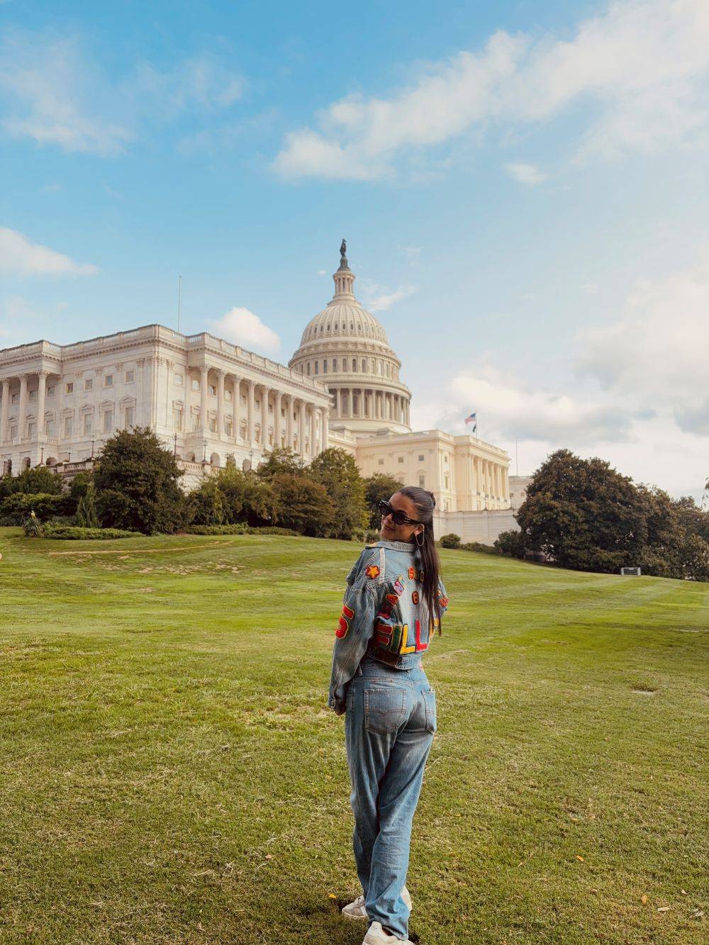 Girl au pair in front of the White House in Washington D.C., posting with her back against the camera, looking over her shoulder. She is wearing a jeans shirt and jeans trousers in the same colour, with a few red details on her jeans shirt.