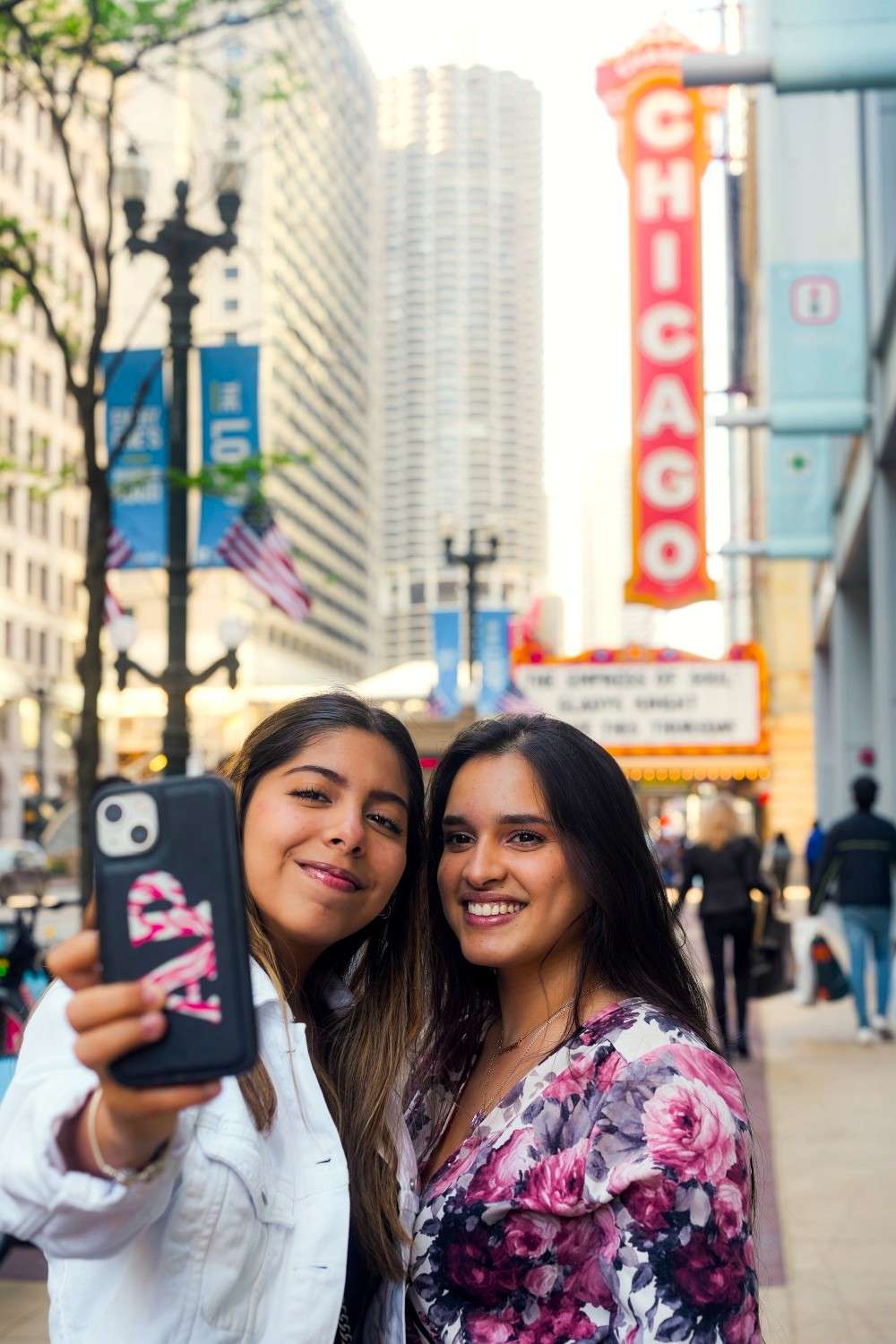 Two women smiling for a selfie in a city street with the famous Chicago Theater sign in the background.
