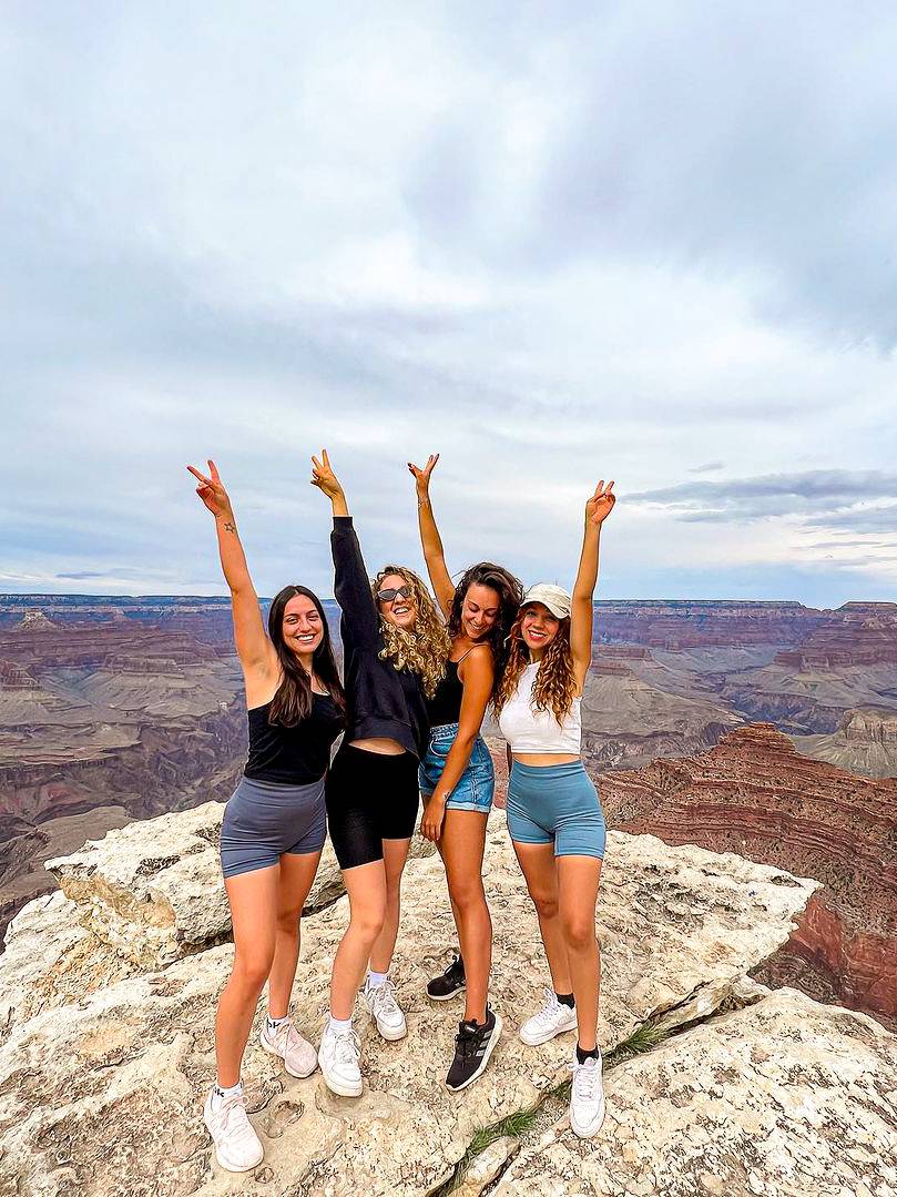 Four women stand on a rocky cliff at the edge of a canyon.