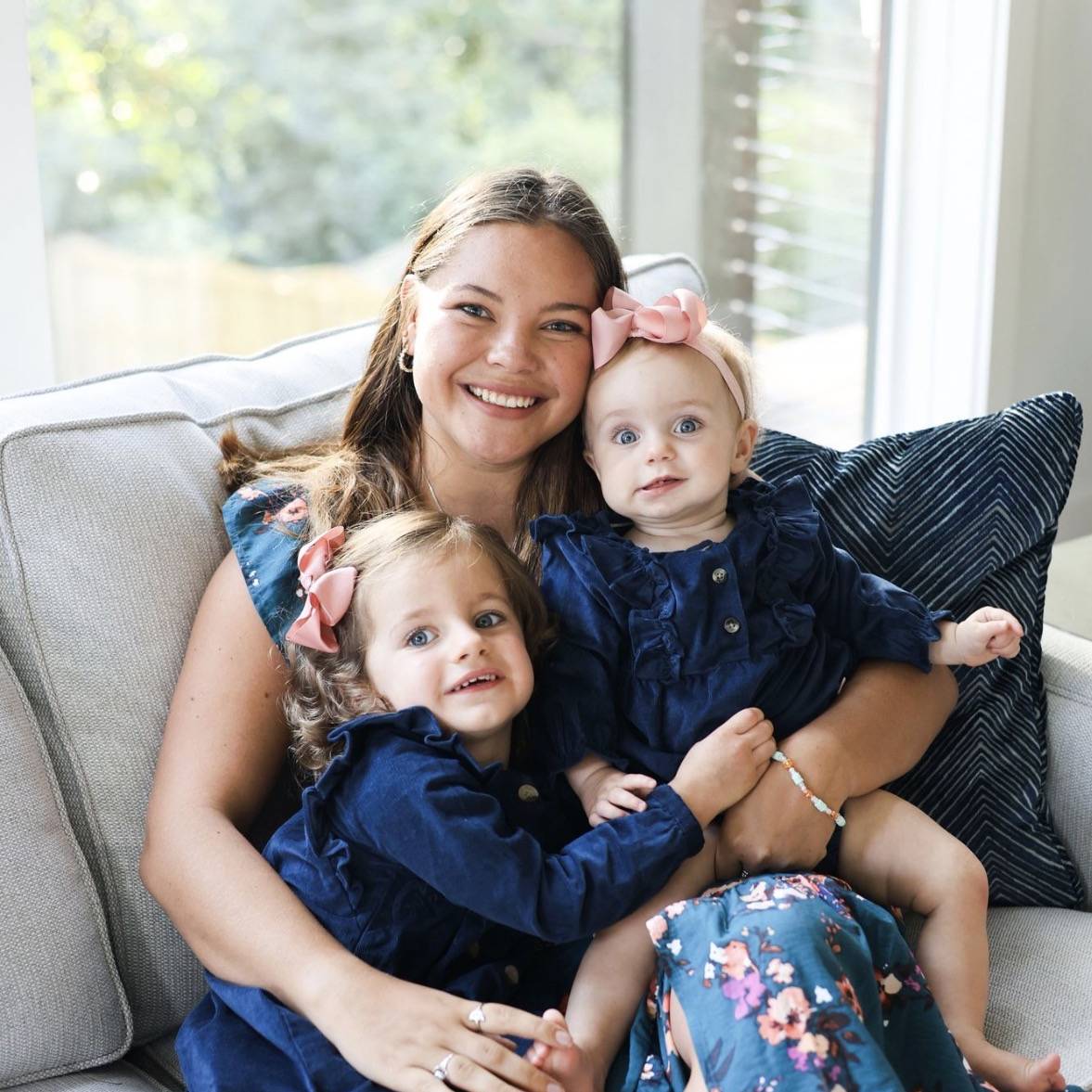 Au pair sitting in couch with two small children, girls in her lap.