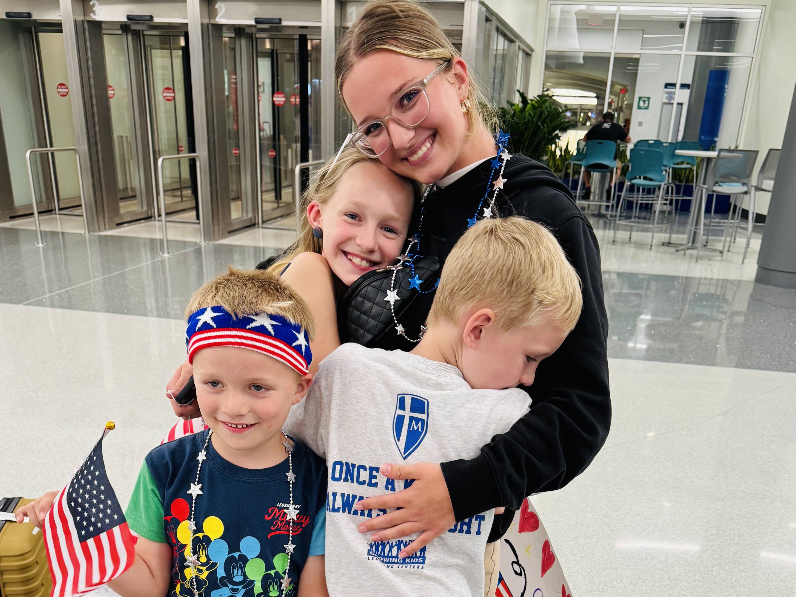 A smiling woman hugs three children in an airport.