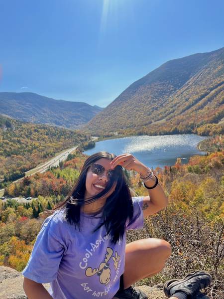 Girl infornt of forest covered mountains and a lake.