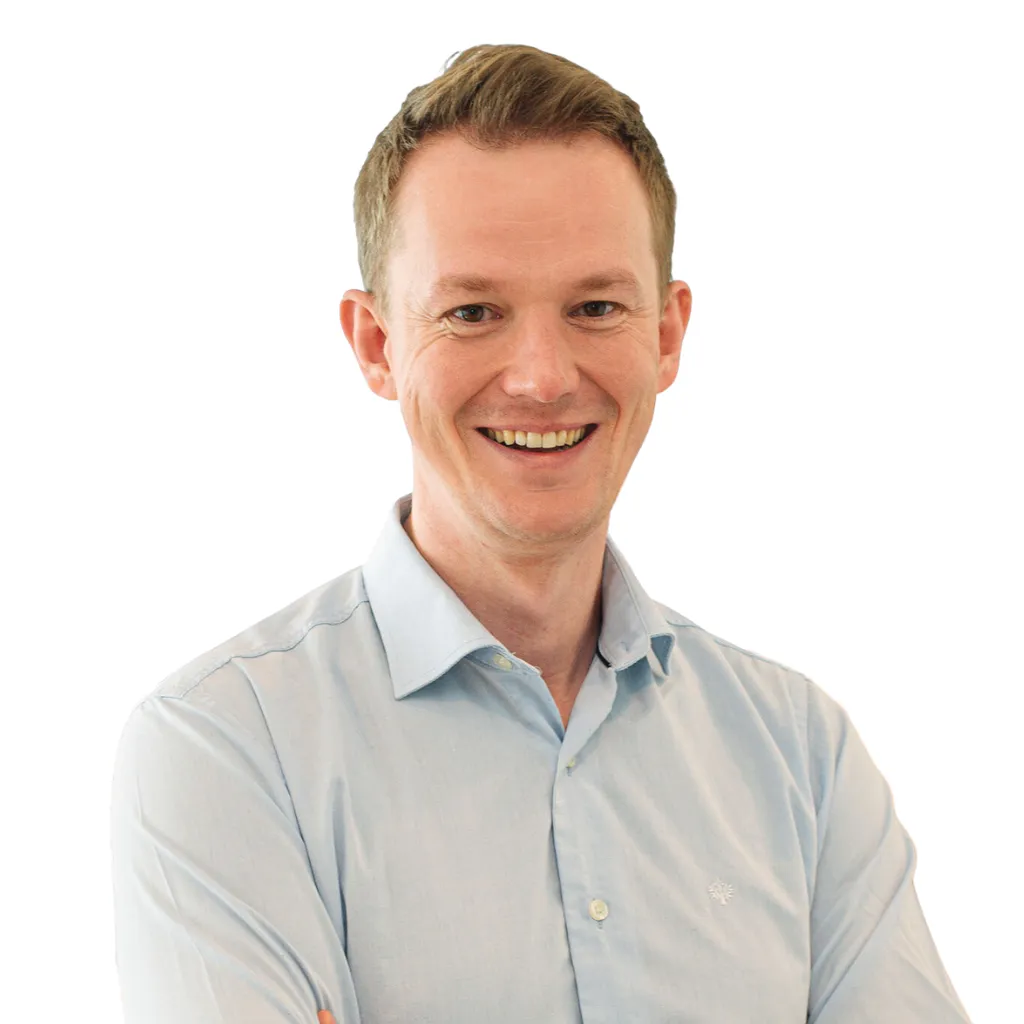 Smiling man in a light blue shirt with arms crossed, standing against a plain white background.
