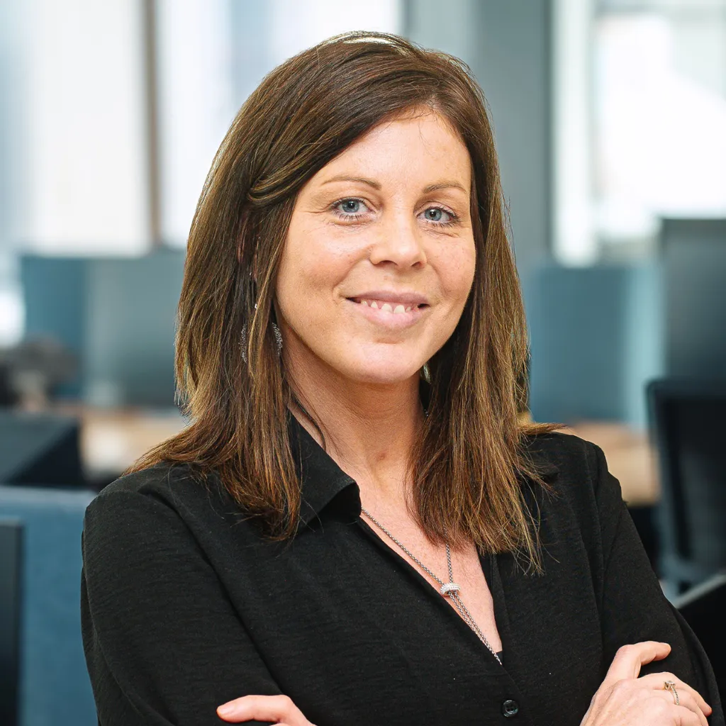 Smiling professional woman with crossed arms in a modern, bright office setting.