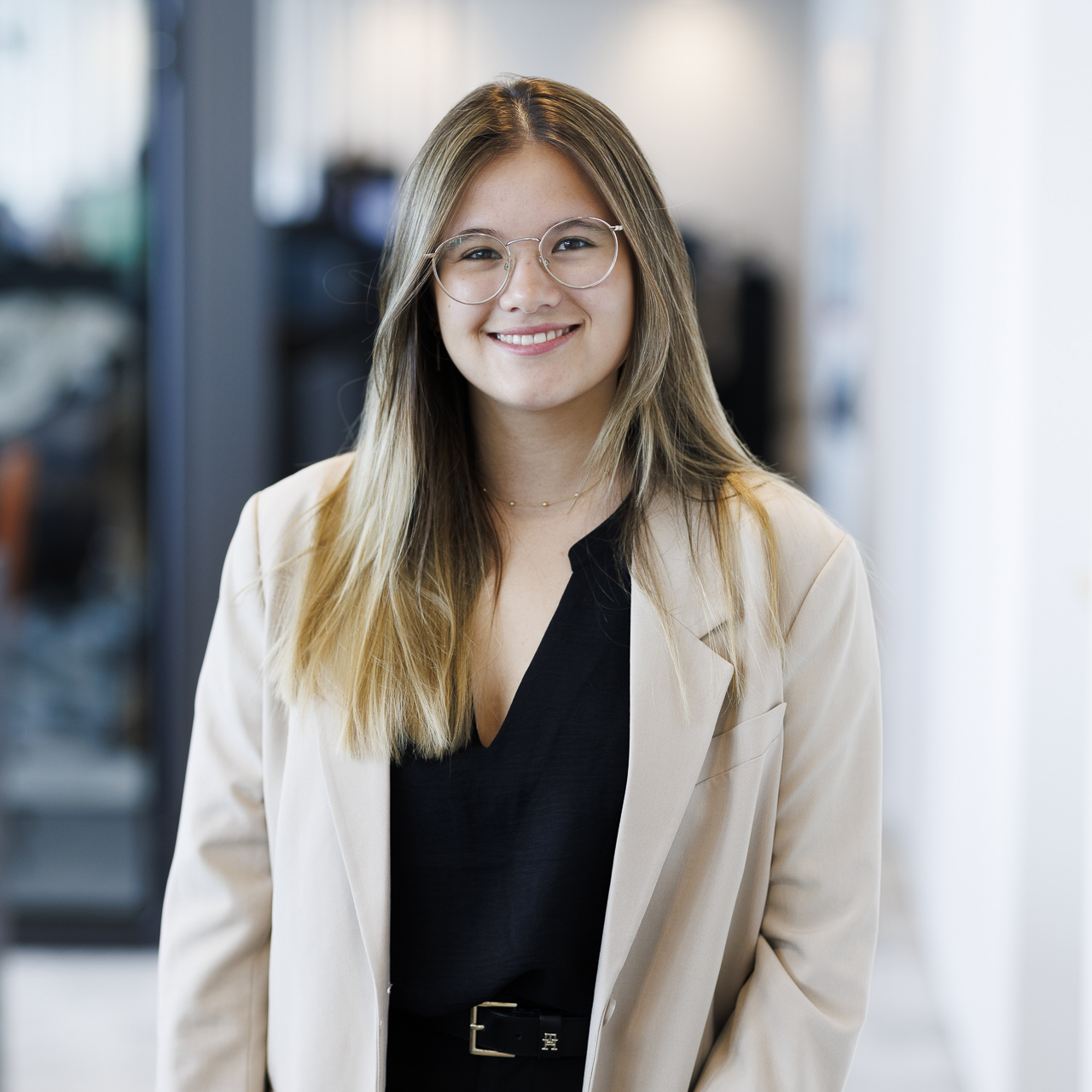 A professional woman in a suit and glasses stands confidently in a modern office environment.