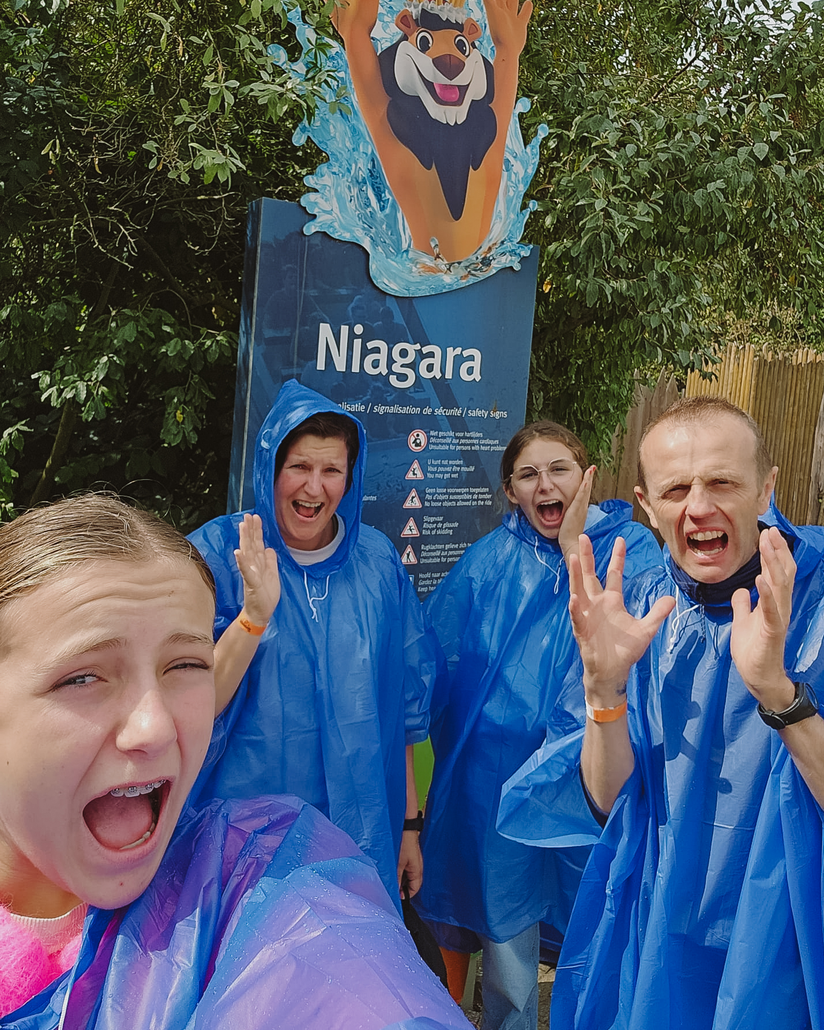 Four people in blue ponchos posing excitedly in front of a 