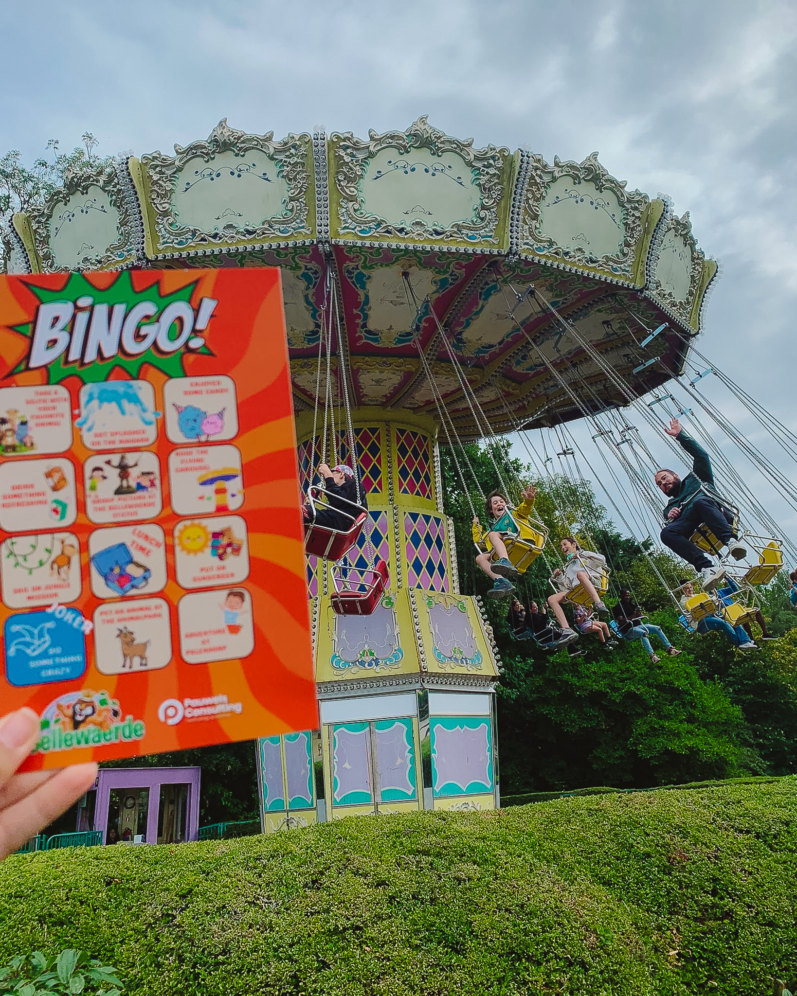 A colorful swing ride at an amusement park with people enjoying the ride, and a hand holding a 