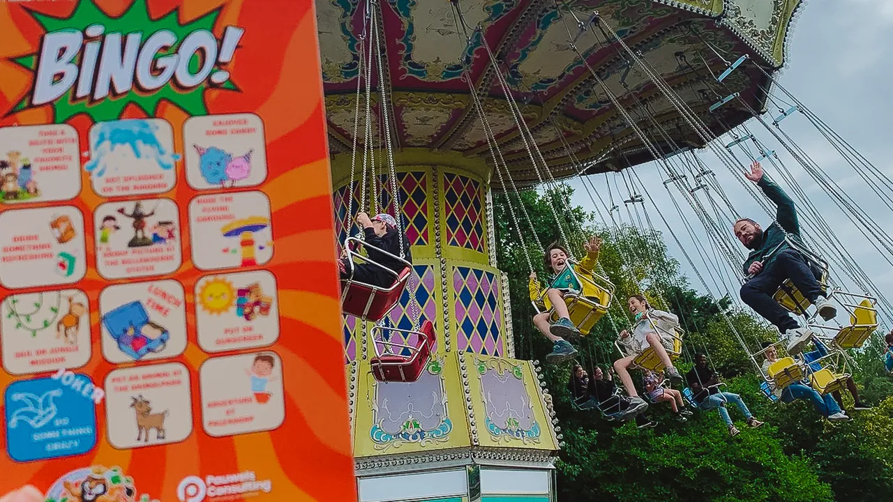 A colorful swing ride at an amusement park with people enjoying the ride, and a hand holding a "Bingo!" card in the foreground.