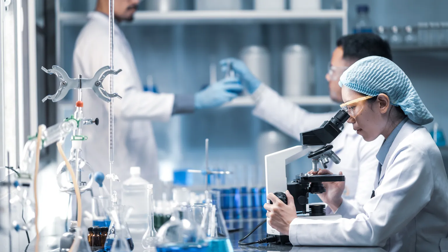 Two scientists in lab coats examining samples under a microscope in a laboratory setting.