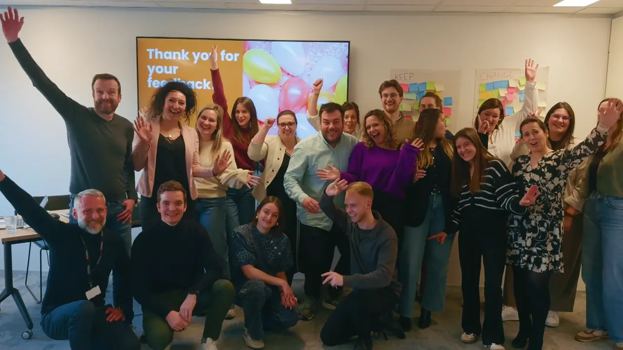 A group of individuals smiling and posing together in front of a large screen displaying vibrant visuals.
