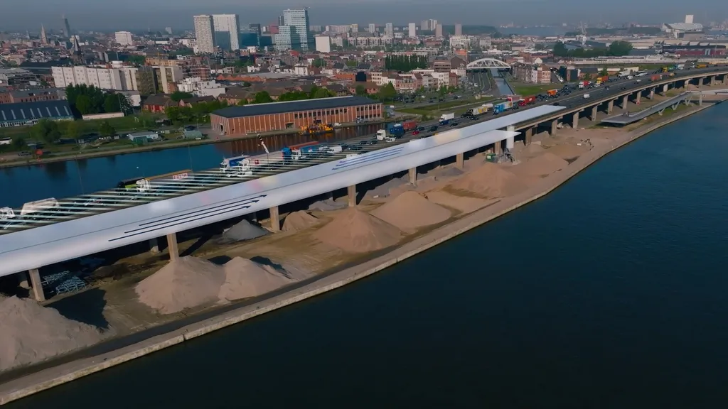 A rendered aerial view of the Oosterweel infrastructure project in Antwerp, Belgium, showing a modern highway bridge with a covered traffic lane running alongside an industrial canal, surrounded by a cityscape with high-rise buildings.
