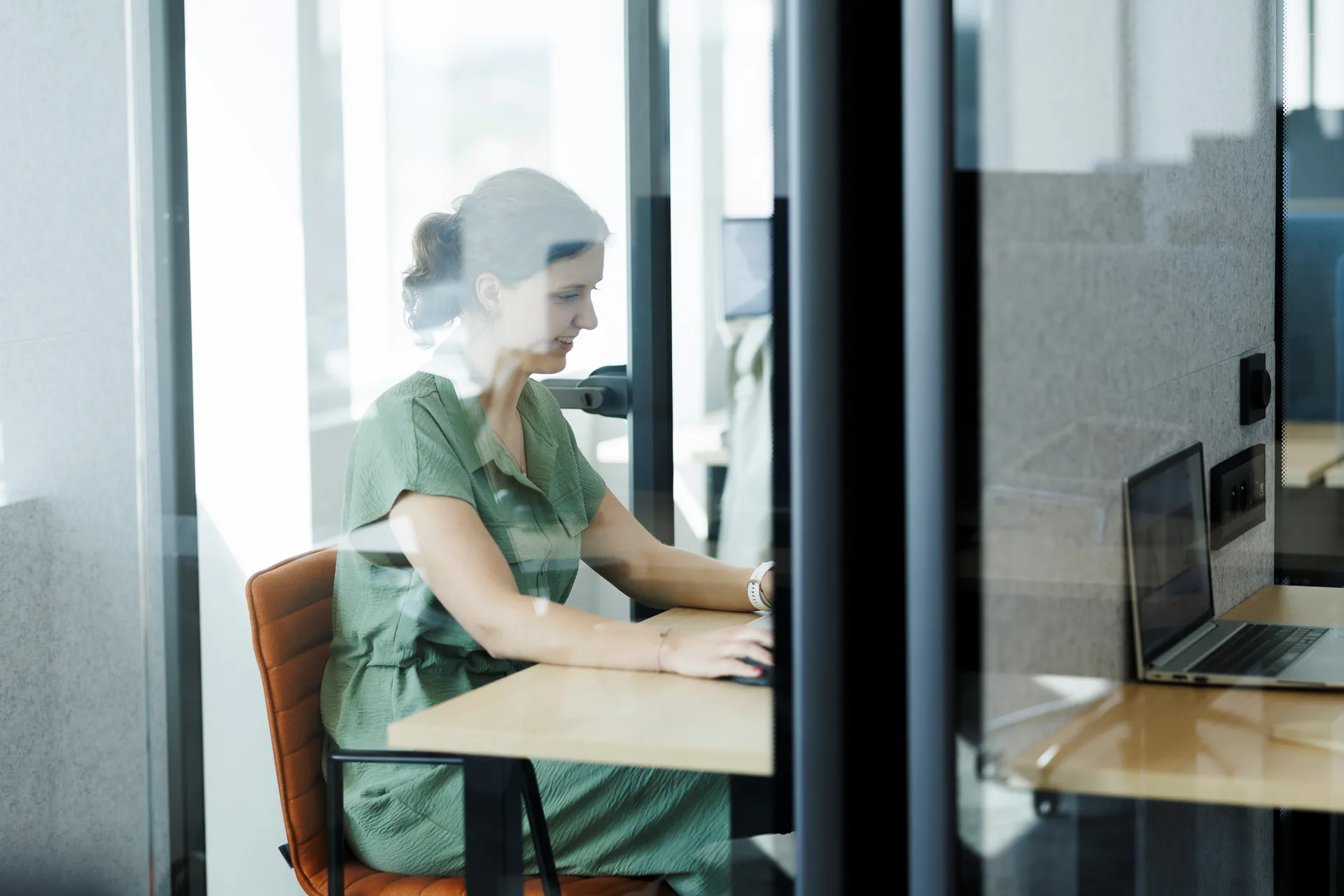 Woman sitting in a phone booth working on her laptop