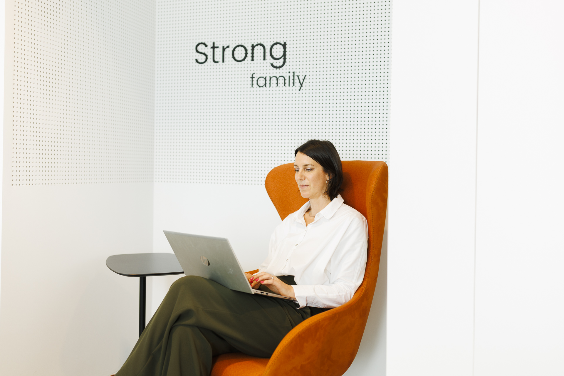 Strong family on wall quote with colleague working on her laptop in orange chair.